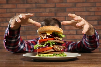 Hungry man and huge burger on table