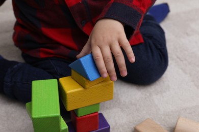 Little child playing with building blocks on carpet, closeup