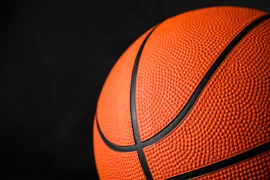 Closeup view of orange ball on black background, space for text. Basketball equipment