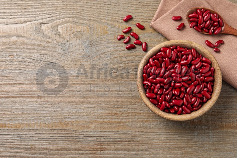 Raw red kidney beans with bowl, spoon and napkin on wooden table, flat lay. Space for text