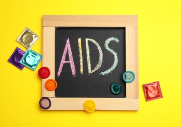 Colorful condoms and blackboard with word AIDS on yellow background, flat lay. Safe sex