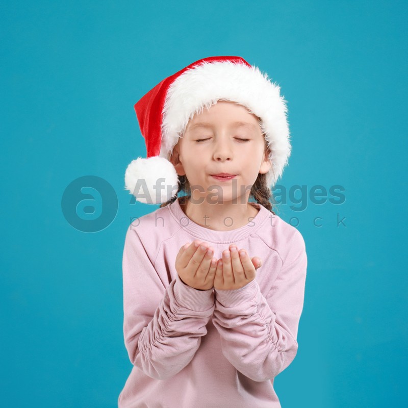 Little child in Santa hat on light blue background. Christmas celebration