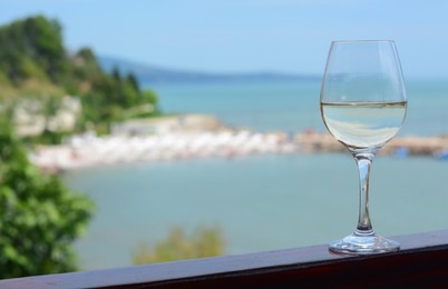 Glass with wine on railing near sea. Space for text