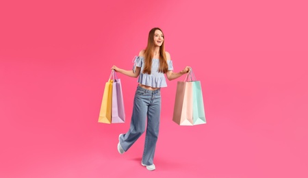 Beautiful young woman with paper shopping bags running on pink background
