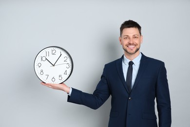Happy businessman holding clock on grey background. Time management