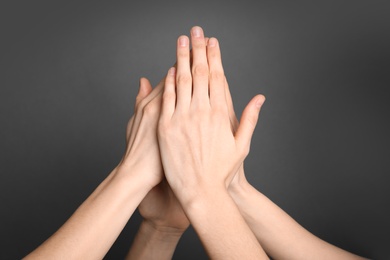 Group of young people giving high five on grey background, closeup. Victory concept