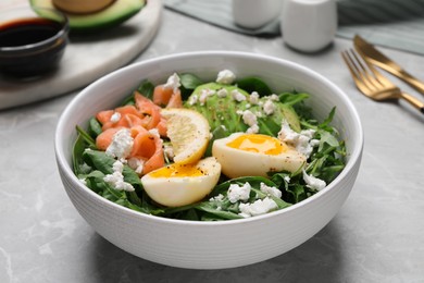 Photo of Delicious salad with boiled egg, salmon and cheese in bowl on light grey marble table, closeup