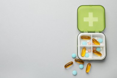 Plastic box with different pills on light grey background, flat lay. Space for text