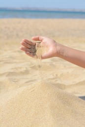 Child pouring sand from hand on beach, closeup. Fleeting time concept
