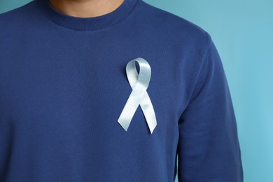Photo of Man with ribbon on light blue background, closeup. Urology cancer awareness