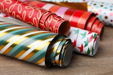Different colorful wrapping paper rolls on wooden table, closeup