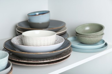 Different clean plates and bowls on shelf in cabinet, closeup