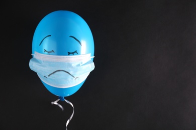 Air balloon in medical mask with drawn sad face on black background. Space for text
