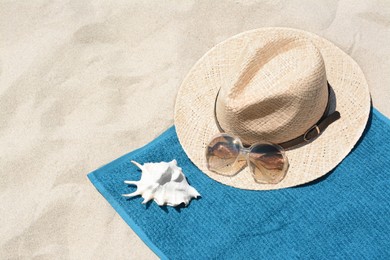 Soft blue towel, sunglasses, straw hat and seashell on sandy beach