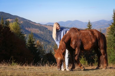 Photo of Young woman petting beautiful horse in mountains on sunny day