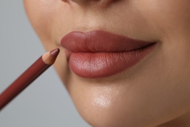 Photo of Young woman applying beautiful nude lip pencil on light grey background, closeup