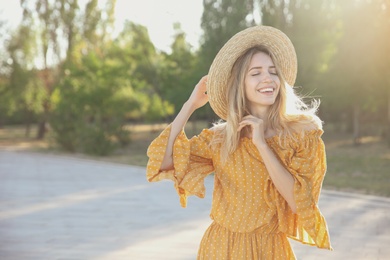 Beautiful young woman in stylish yellow dress and straw hat outdoors