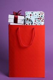 Photo of Red paper shopping bag full of gift boxes on purple background