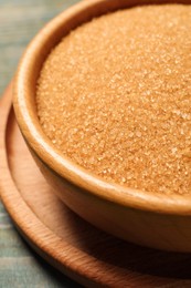 Brown sugar in bowl on light blue wooden table, closeup