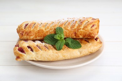Photo of Fresh tasty puff pastry with sugar powder and mint on white wooden table, closeup