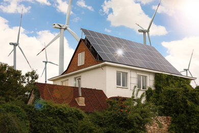 Wind turbines near house with installed solar panels on roof. Alternative energy source