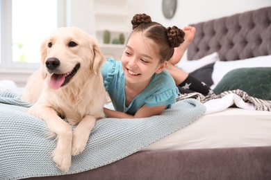 Photo of Cute little child with her pet on bed at home