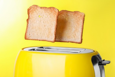 Modern toaster with roasted bread against yellow background, closeup