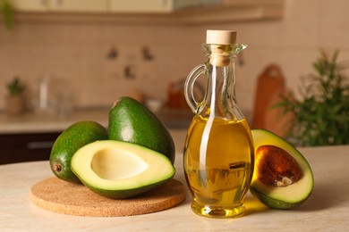 Photo of Fresh avocados and jug of cooking oil on beige marble table in kitchen