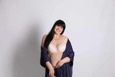 Beautiful overweight woman in beige underwear and silk robe on light background. Plus-size model