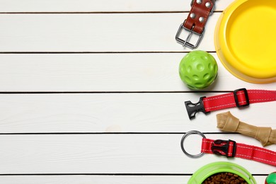 Flat lay composition with dog collars, toys and bowl on white wooden table. Space for text