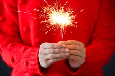 Woman in red sweater holding burning sparklers, closeup