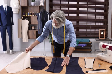 Photo of Professional tailor working with fabric at table in atelier