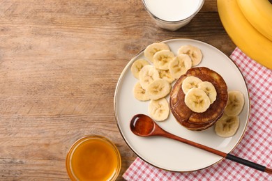 Plate of banana pancakes with honey on wooden table, flat lay. Space for text