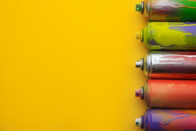 Used cans of spray paints on yellow background, flat lay with space for text. Graffiti supplies