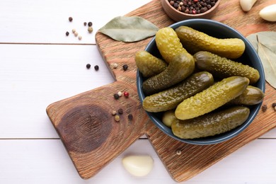 Photo of Tasty pickled cucumbers in bowl and ingredients on white wooden table, flat lay