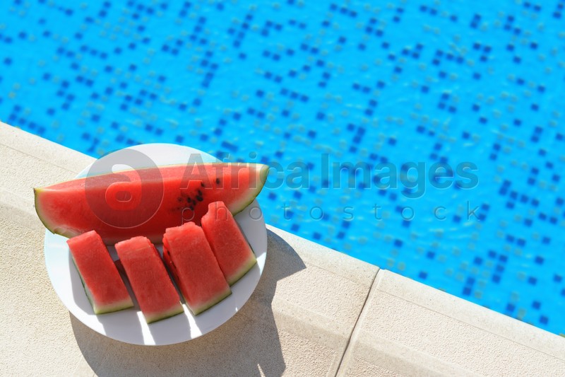 Slices of watermelon on white plate near swimming pool outdoors, top view. Space for text