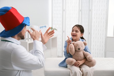 Pediatrician in funny hat playing with little girl during visit at hospital