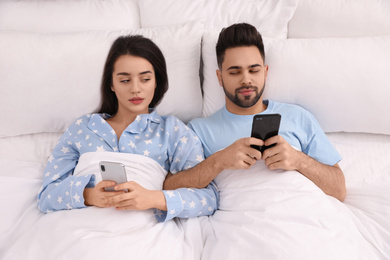 Distrustful young couple peering into each other's smartphones in bed at home, above view