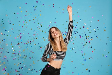 Happy woman and falling confetti on light blue background