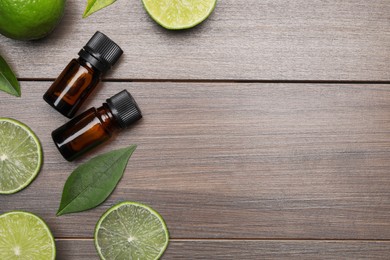 Bottles of essential oil with lime slices and leaves on wooden table, flat lay. Space for text