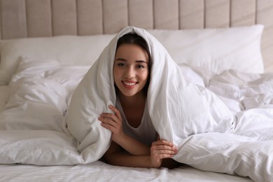 Photo of Cheerful young woman covered with warm white blanket lying in bed