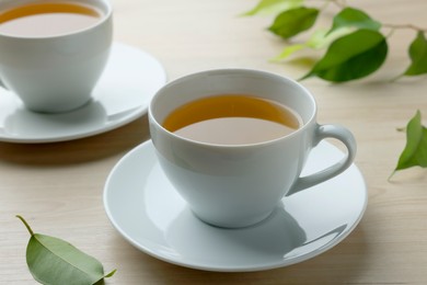 Photo of Green tea in white cups with leaves on wooden table, closeup