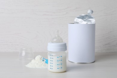 Blank can of powdered infant formula with scoop and feeding bottle on white wooden table. Baby milk