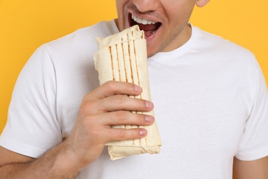 Photo of Man eating delicious shawarma on yellow background, closeup