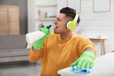 Man with spray bottle and rag singing while cleaning at home