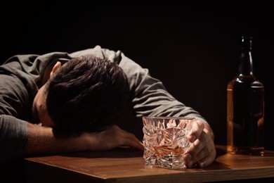 Addicted man with glass of alcoholic drink at wooden table against black background