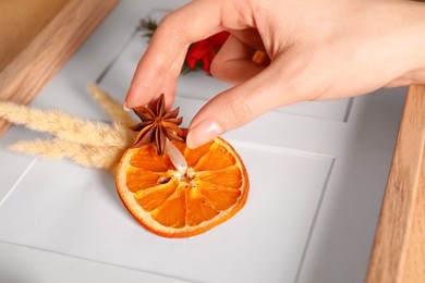 Photo of Woman making Christmas decor with dry orange slice at wooden table, closeup