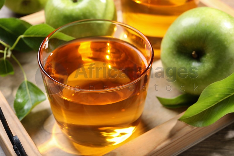 Glass of fresh apple juice on wooden tray, closeup