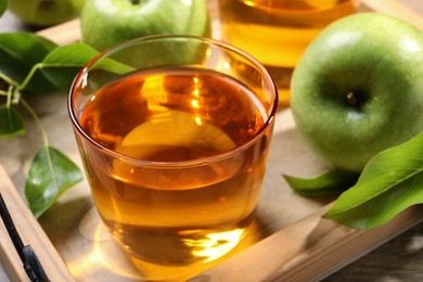 Photo of Glass of fresh apple juice on wooden tray, closeup