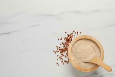 Buckwheat flour in bowl with wooden spoon on white marble table, flat lay. Space for text